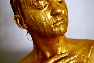 A woman’s head and shoulders are shown, covered completely in golden colour