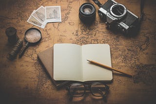 There is a notebook, pencil, old camera, glasses, and magnifying glasses on an old map.