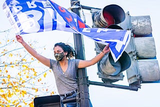 young woman standing tall waving a Biden for president flag