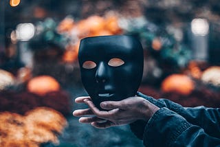 A black theatre mask held by two hands.