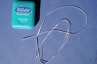 A light blue dental floss container sits next to a strand of dental floss.