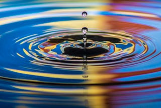 A ripple effect created by a stone dropping in water — we see the stone and its colorful ripple effects in water