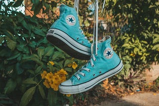 Close up of a pair of light turquoise Converse baseball boots, hanging on a washing line.