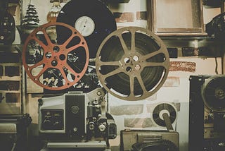 A vintage display featuring film reels, a vinyl record, and an old projector, set against a textured wall