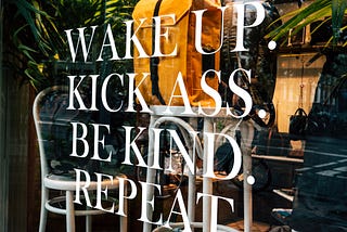 Wake up. Kick ass. Be Kind. Repeat. Quote written on coffee shop window.