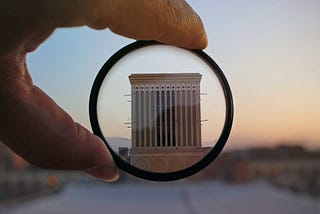 Research section: A magnifying glass held up to show a building as everything on the outside of the glass is blurred out to focus on only the centre of the image where the structure lies.