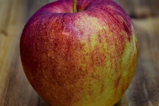 A red apple, possibly a Gala, possibly organic, on a table