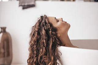 A woman relaxes in a tub with her hair trailing over the edge