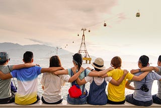 8 children seen from the back, holding themselves by the shoulder to symbolize diversity and friendship, looking at the ocean