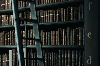 A black wooden ladder leaning to the left in front of book shelves made of black wood.