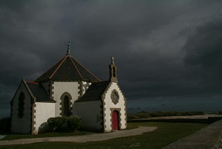 A small, isolated church, against a brooding sky of ominous, dark clouds