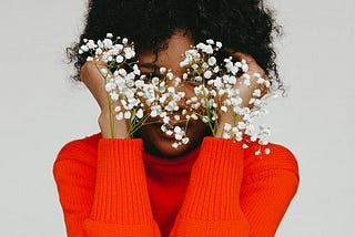 Image of a woman in a bright red top with flowers covering her face.