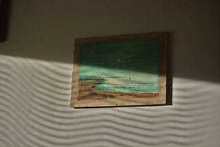 A seaside painting is obscured by wavy shadows on a wall.