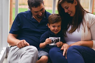Young boy sits between his parents holding a baby ultrasound image.