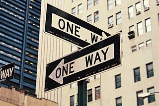 Two one-way signs on a street corner pointing in opposite directions