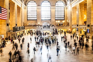 A crowd of people moves through a large, open train station