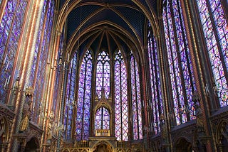 inside of a cathedral, with tall arches holding up stained glass windows