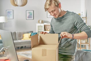 Young man opening a box next to his computer monitor.