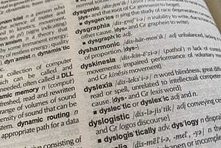 Photograph of a dictionary page from a slanted angle showing the partial definition for dyslexia. The visible part of the definition includes the words: “word blindness” and “unrelated to intellectual competency.”