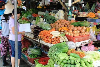 A couple of customers consider the fruit and vegetables on display at a market stall.