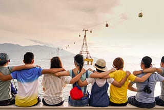 A group of people with arms around each other looking out into the ocean