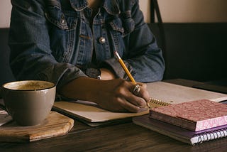 Woman writing in notebook with coffee cup and notebooks on table