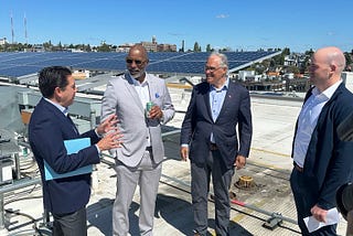 Group of four people standing on a rooftop in front of solar panels