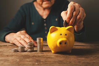 An older person puts coins in a money piggy bank