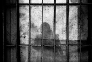 An image of a dark shadow of a woman seen through prison bars on the wall.