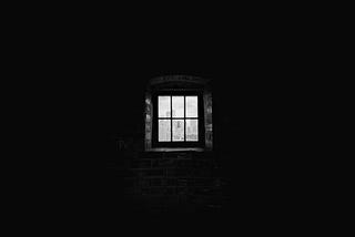 A small solitary barred window in a dark room