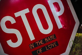 A close up of a stop sign that has “in the name of love” written underneath it.