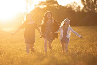 Three girls running through a field at sunset