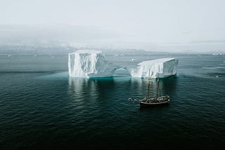 A sailing ship anchored near a massive melting iceberg