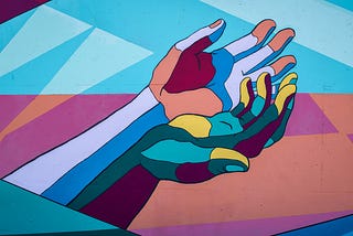 Two hands join together to represent solidarity with individuals who experience mental health challenges in a mosaic of bright colors.