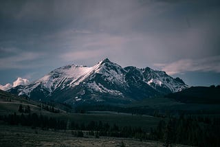 A dramatic mountain landscape featuring snow-capped peaks under a moody sky.