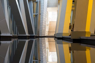 A mirrored floor reflecting steel beams and yellow beams.