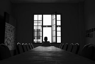 black and white photo of a person alone at a table with ten empty chairs