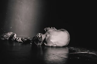 A black and gray image of a man self soothing on the floor, clearly he’s in pain