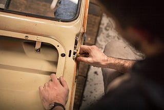 A worker applies what seems to be steel wool to a mechanism on the inner body of a freshly painted automobile.