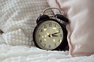 An old fashioned alarm clock sits on a cozy bed.