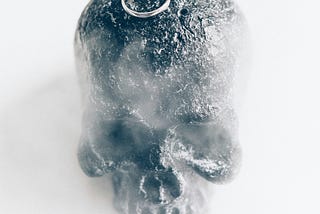Wedding rings sitting on a rock skull surrounded by mist.
