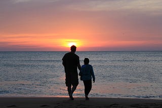 man and girl/young woman walking into a watery sunset with their backs to the camera