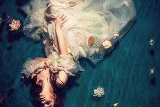 A woman dressed in a white dress floating in the water on her back.