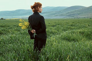 Young red-haired woman standing in a country field holding goldenrod behind her back