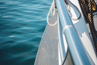 The front of a boat shining in the sun as it sails through deep, blue water.