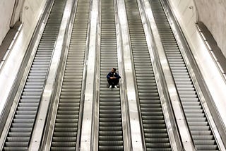 A young man sits on an empty escalator