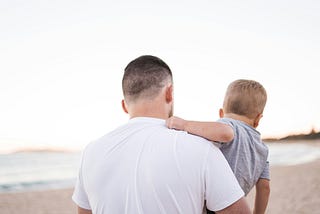 Father carrying his son while they walk on a beach
