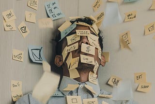 A man’s face and area around it covered with blue and yellow sticky notes on which words and symbols related to tiredness are mentioned.