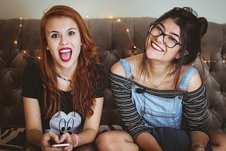 Two teen girls smiling and sitting on a couch