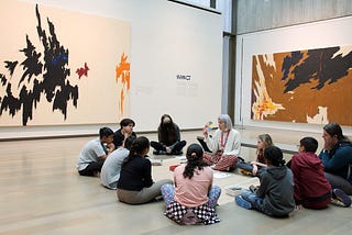 An educator and children sit in a circle on the floor in a gallery during an Instill lesson.